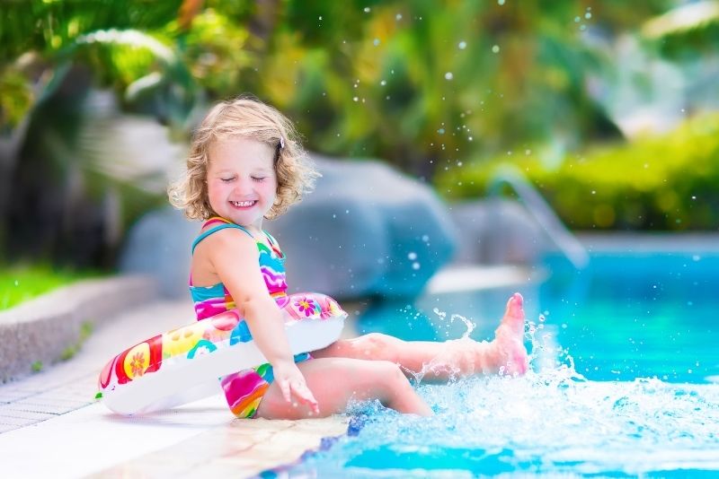 a smiling kid with a floater beside the swimming pool