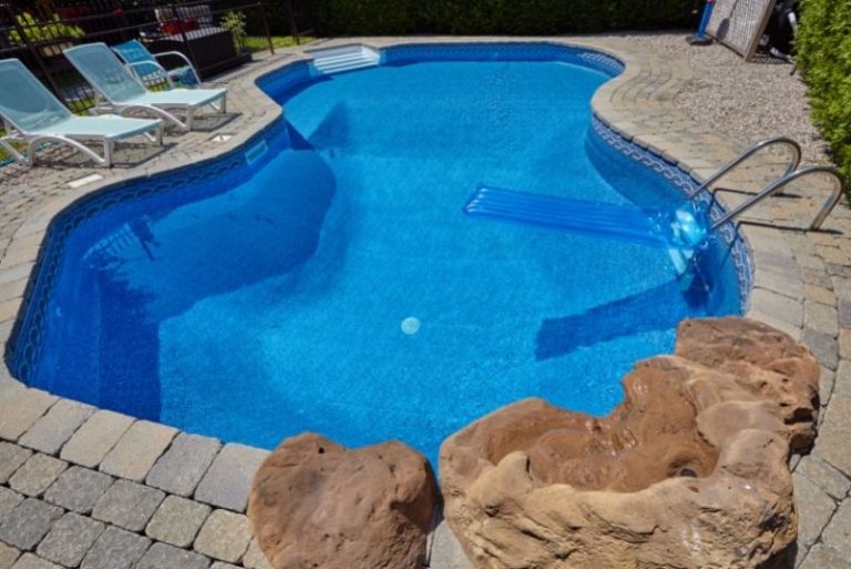 Freeform curved swimming pool with a pool lounger and paved surround